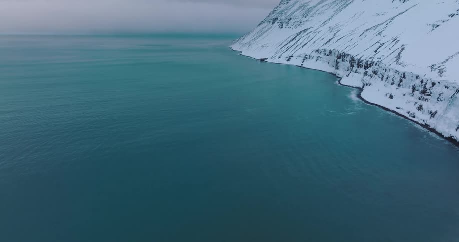 A stunning aerial view captures the dramatic contrast between a snow-covered coastline and the tranquil turquoise ocean