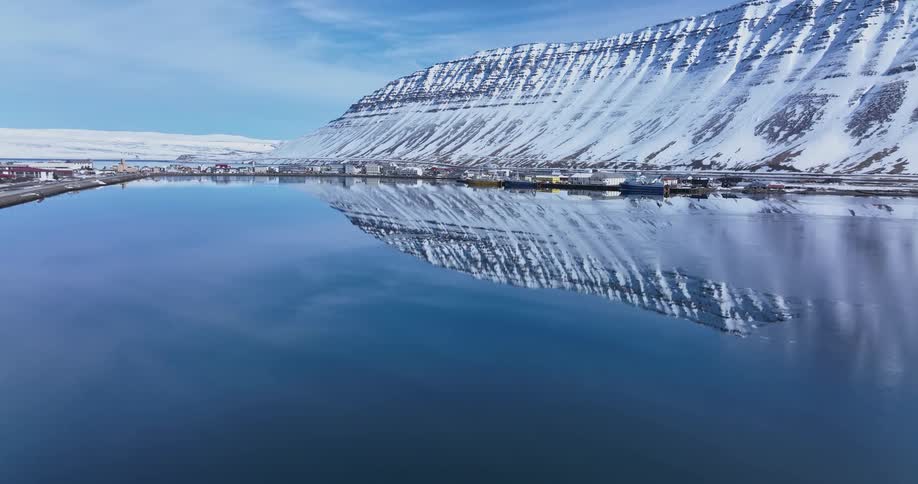 Cinemagraph of a majestic snow-covered mountain perfectly reflected in a tranquil fjord by a coastal village