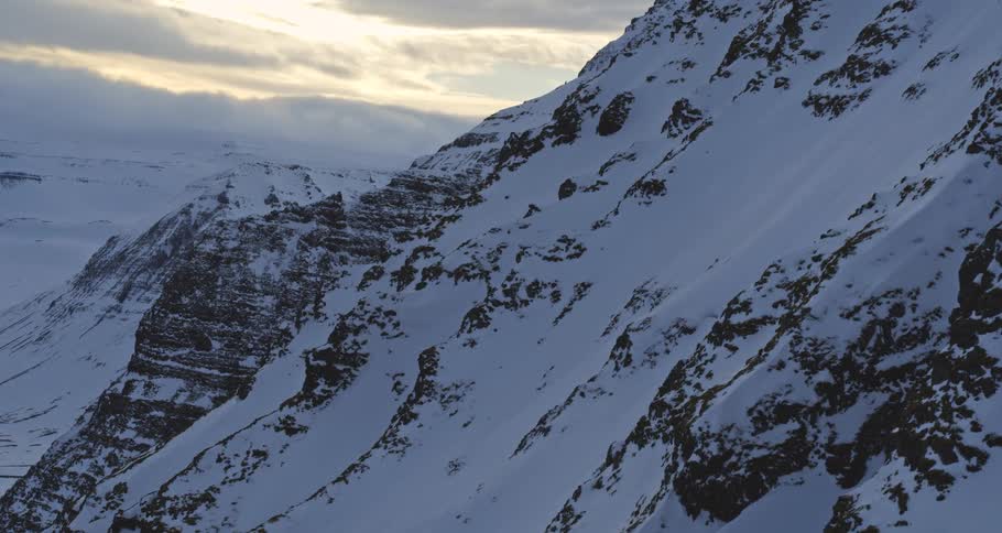 An aerial view slowly pulls back to reveal the impressive scale of a steep, snow-dusted mountainside