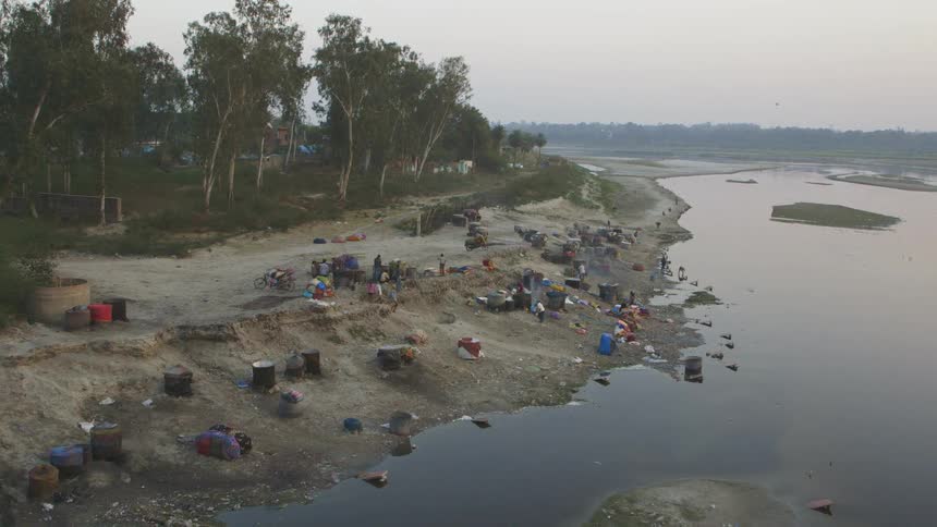 People walking towards, and away from, a shoreline littered with barrels