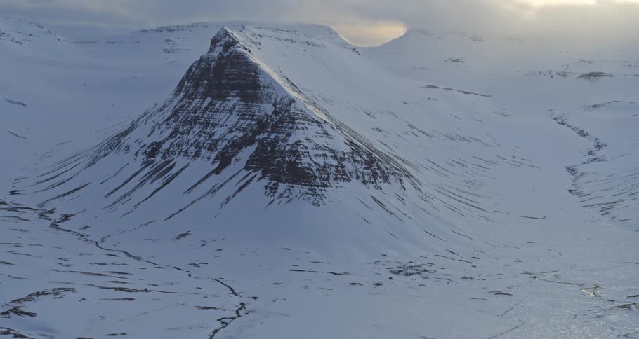 A stunning time-lapse of sunlight and shadows moving across a majestic snow-covered mountain and frozen landscape as clouds drift overhead