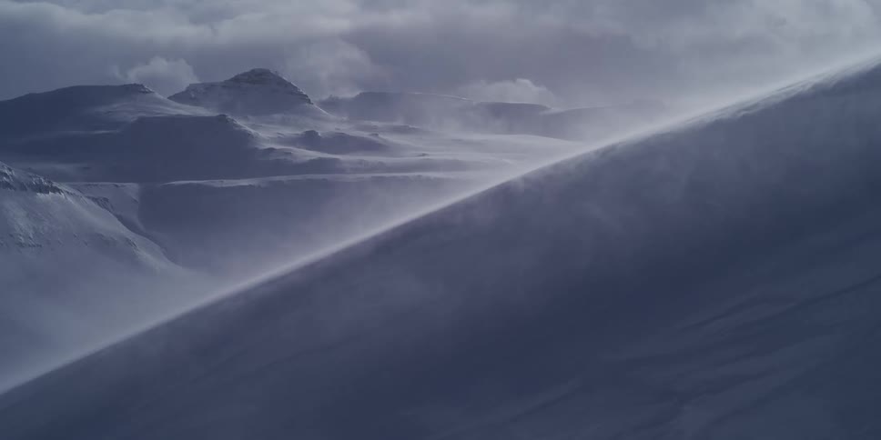 Intense winds blow snow across a vast, frozen mountain landscape during a powerful blizzard