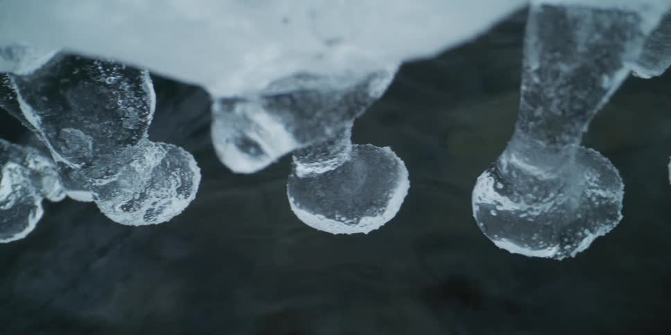 A mesmerizing close-up of peculiar ice formations hanging just above a dark, flowing stream in winter