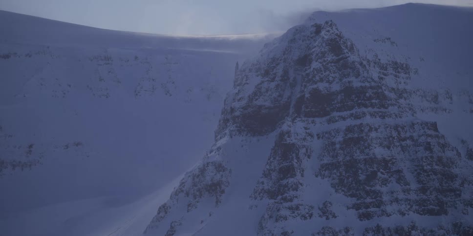 Fierce winds whip snow across a vast, frozen mountain landscape during a blizzard