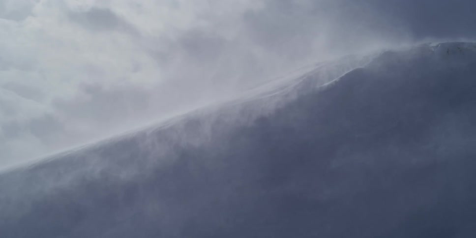 Fierce winds blow snow in slow motion over a mountain ridge during a powerful blizzard