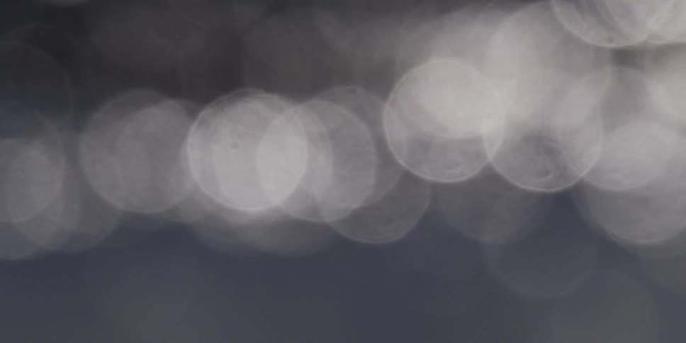 Cool-toned bokeh light reflections shimmer and float on a dark, moving surface