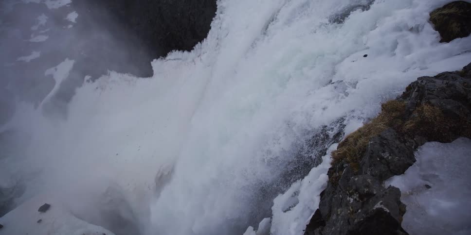 Close up of a powerful, icy waterfall rushing over a cliff in a winter landscape in slow motion