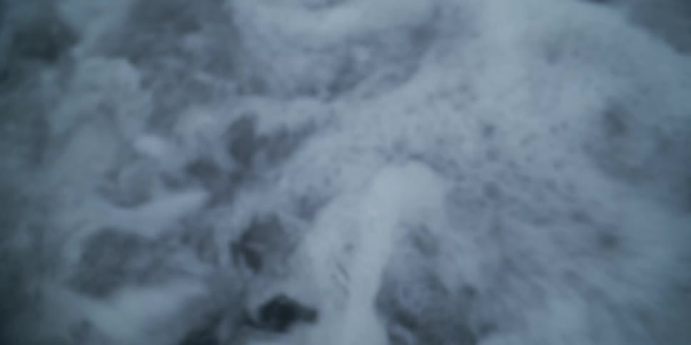 Foamy ocean waves crash over dark rocks on the shore in an extreme slow-motion, out-of-focus shot