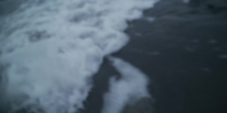 Dreamy, out-of-focus shot of ocean waves gently washing over a rocky shoreline in slow motion