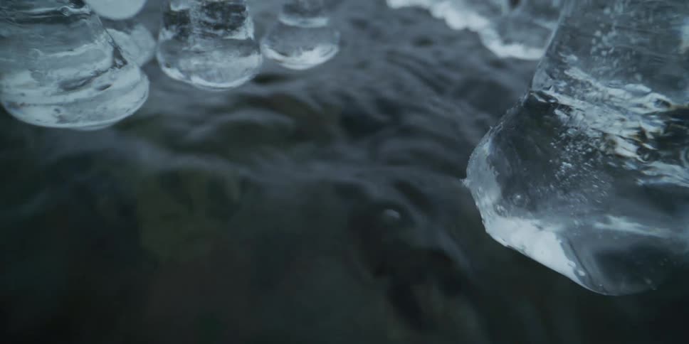 An eerie close-up shot reveals a dark, fast-moving stream with icicles hanging just above the surface