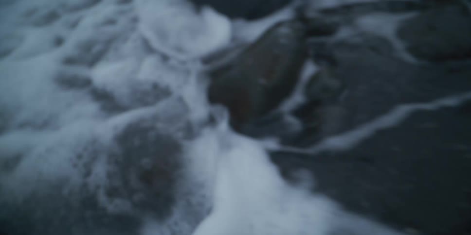 A blurry, slow-motion close-up of churning, foamy water creates an abstract and chaotic scene