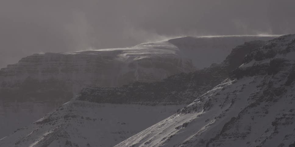 Strong winds blow snow across desolate, snow-covered mountain tops during a harsh winter storm
