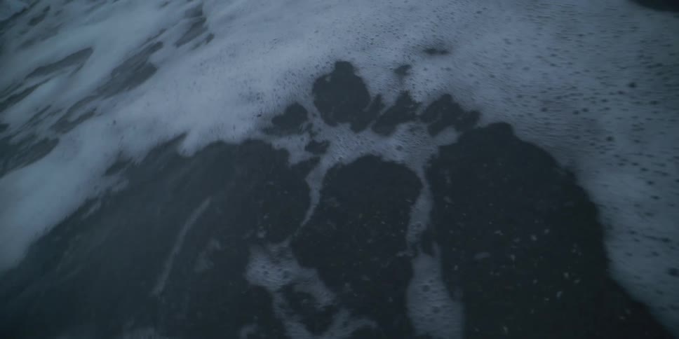 A close-up slow-motion shot of dark, murky water churning and bubbling with white foam