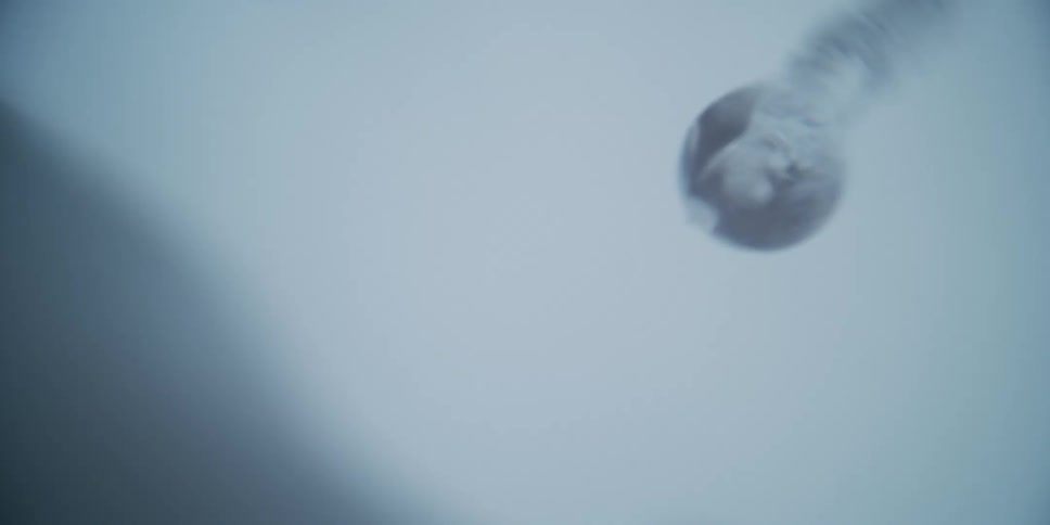 An extreme close-up, slow-motion shot captures a single, clear water droplet forming and falling from its source