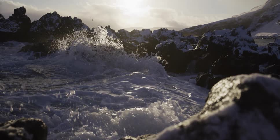Powerful ocean waves crash against snow-covered volcanic rocks in dramatic super slow motion