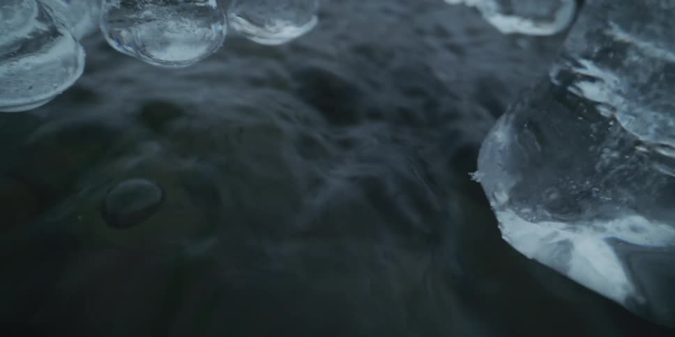 Artistic macro shot of dark, undulating water flowing beneath frozen icicles in slow motion