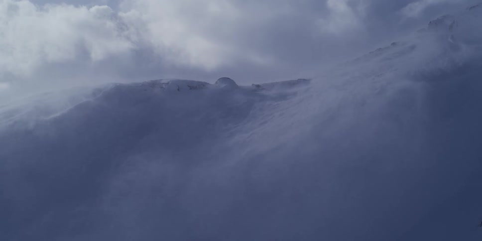 Heavy wind blows snow across a frozen mountain peak during an intense blizzard