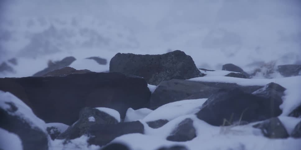 Intense winds blow snow over dark, cold rocks during a winter blizzard