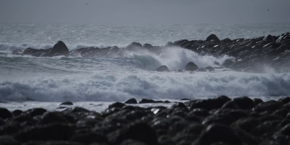 Powerful ocean waves crash over a rocky shoreline in dramatic slow motion