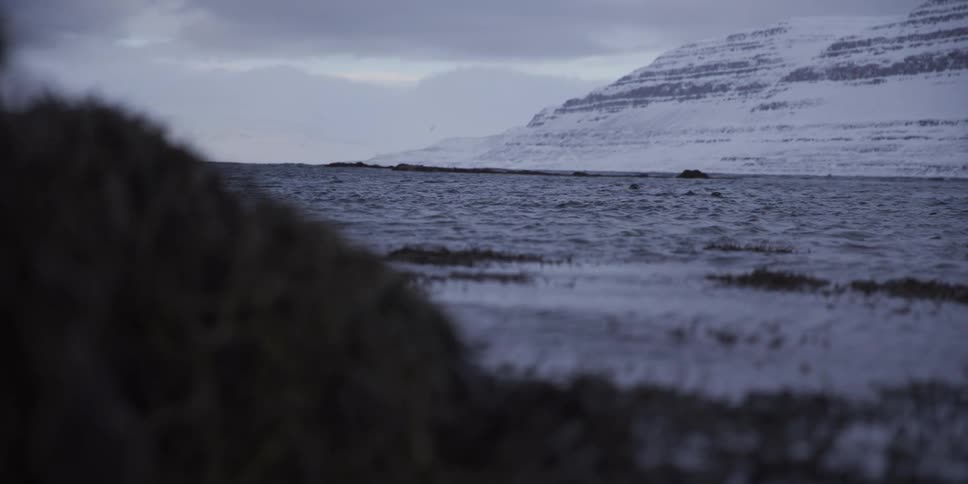 A slow pan reveals a vast and serene winter landscape with a snowy fjord and majestic mountains