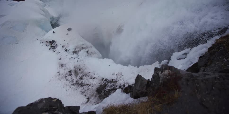 A powerful waterfall crashes through a snowy and icy canyon in a dramatic slow-motion close-up