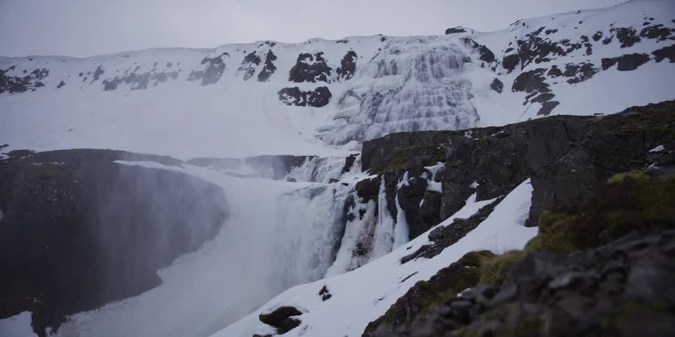 Water rages through a snowy, icy canyon at the base of a majestic frozen waterfall in Iceland