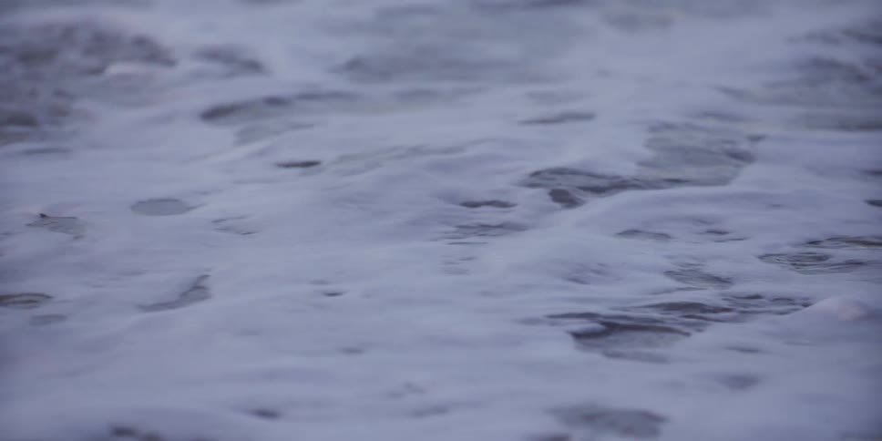 White foam from a gentle ocean wave washes over the sand in a serene slow-motion close-up