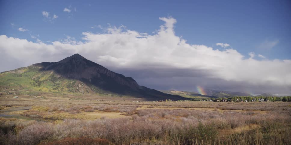 Timelapse of a rainbow appearing as storm clouds part over a majestic mountain valley, revealing a sunlit landscape