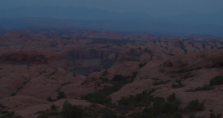 A tranquil aerial view pans slowly over the rugged, red rock desert landscape of Moab, Utah during twilight