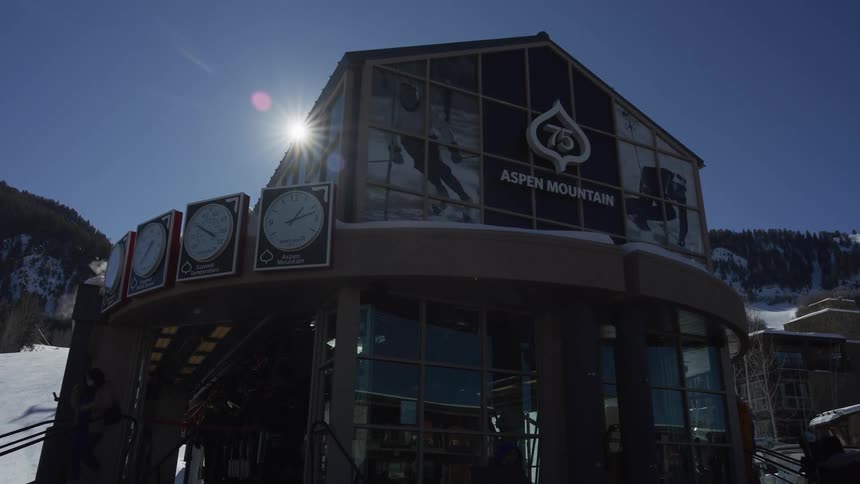 Bright sun shines over the Aspen Mountain gondola station as skiers walk by on a clear day