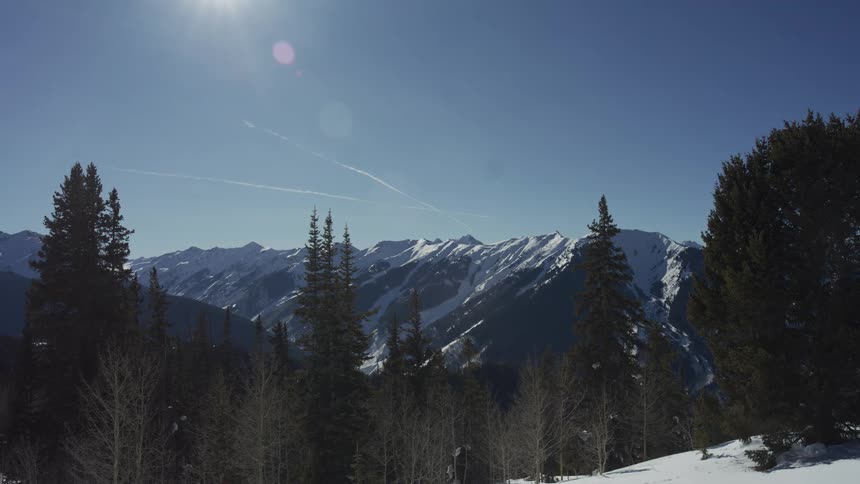 A scenic wide shot of a vast, snow-covered mountain range under a brilliant sun and a clear blue sky