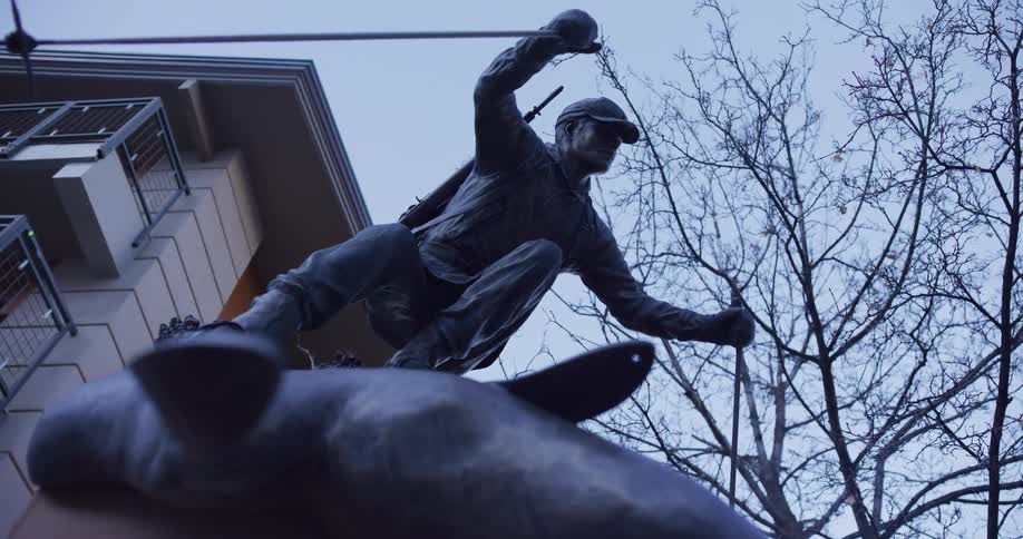 A dramatic low-angle shot captures a bronze statue of a fly fisherman in action against a dusky sky