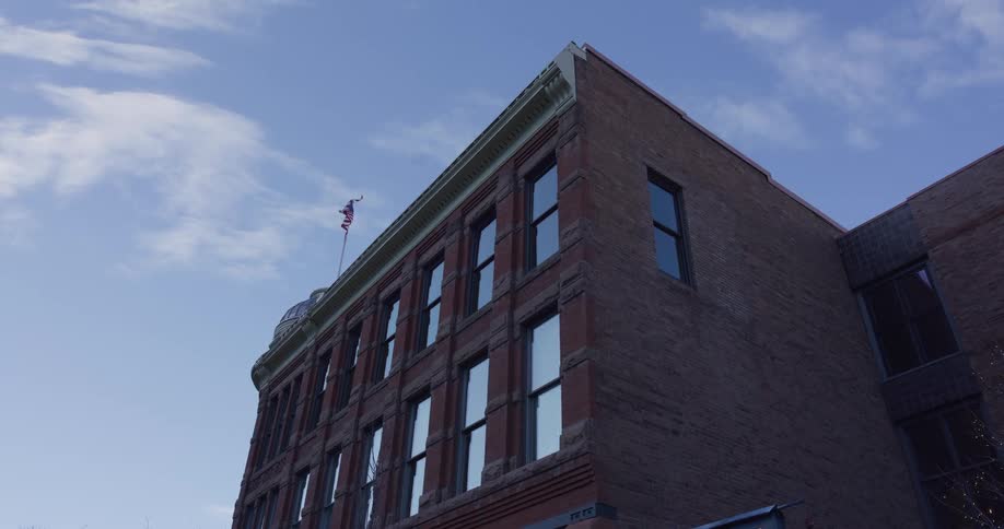 A low-angle shot of a classic red brick building with an American flag waving on the roof against a blue sky
