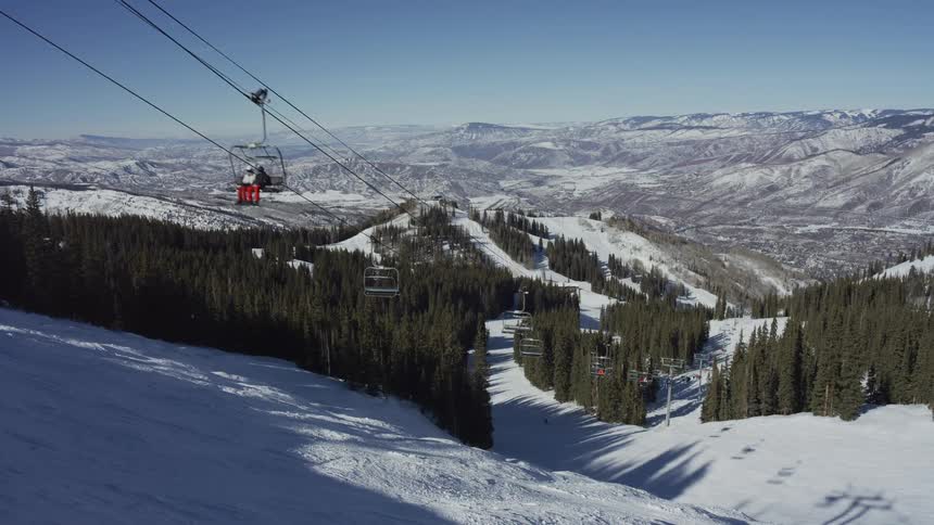 Scenic view from a ski lift looking down on a snowy mountain resort with evergreen trees on a clear sunny day