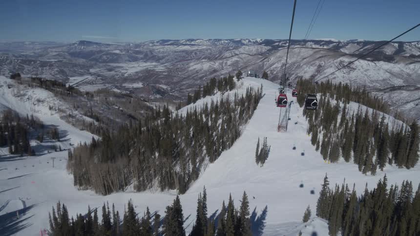 A scenic point-of-view from a gondola ascending over the snow-covered slopes of a ski resort on a bright, sunny day