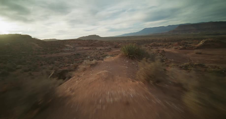 Dynamic FPV drone footage races low across a vast and arid red rock desert landscape