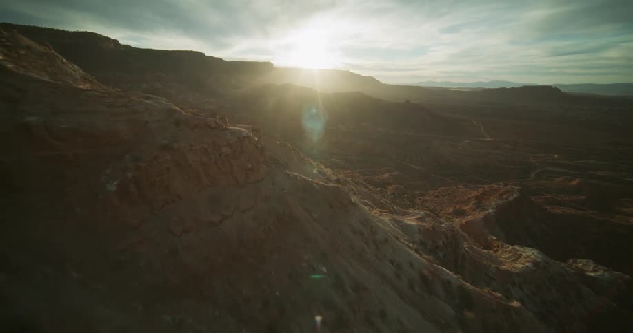 A breathtaking aerial shot slowly flies over a vast desert canyon landscape during a beautiful sunrise