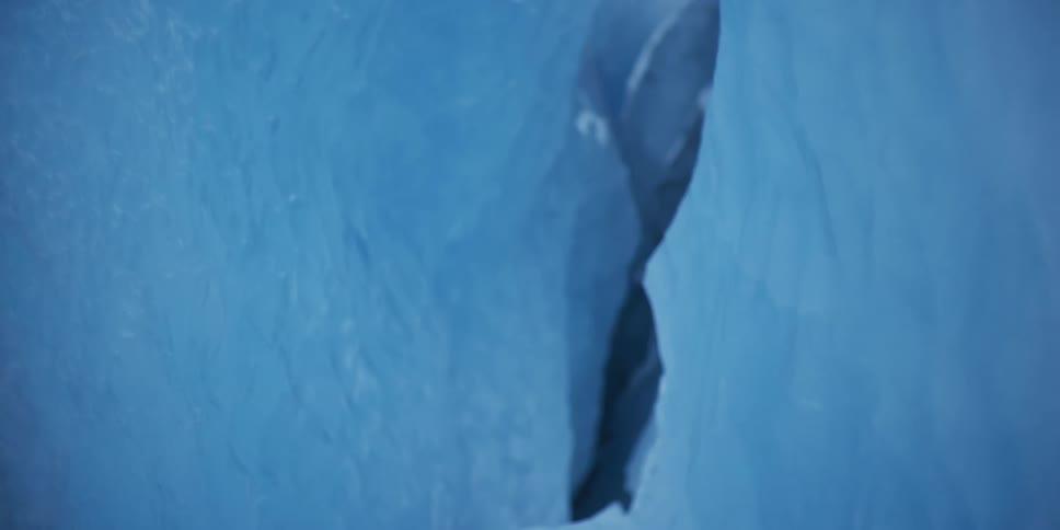 A close-up view of a deep, dark crevasse in a vibrant blue glacial ice wall