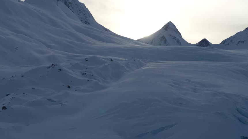 A serene and cold winter landscape unfolds as the camera pulls back over a vast, snow-covered glacier at sunset