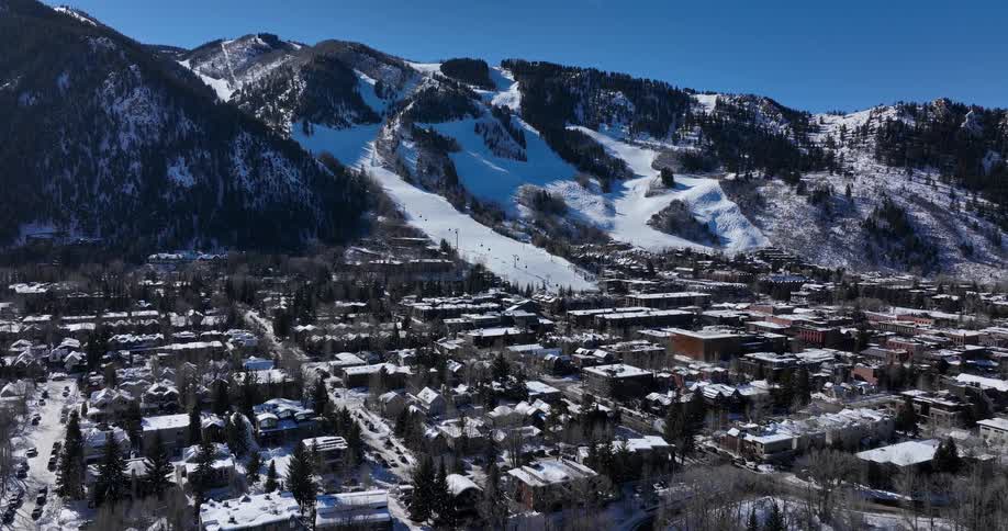 A stunning wide aerial view of the snowy ski town of Aspen, Colorado, at the base of its mountain resort on a clear sunny day