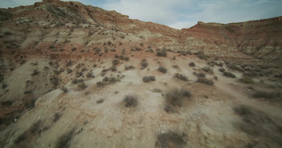An aerial drone shot slowly tracks across the arid and scrubby hillside of a colorful red rock canyon
