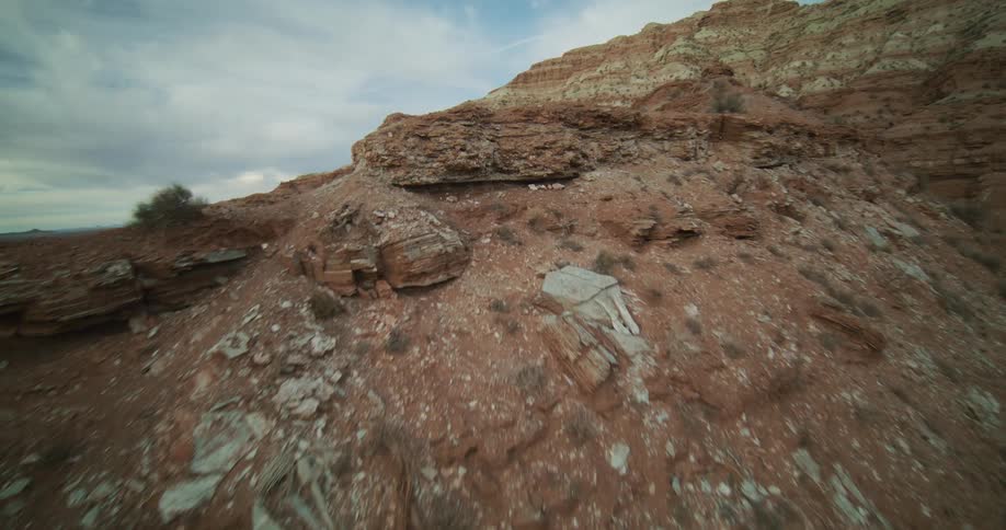 A slow aerial ascent reveals the layered red and white rock formations of a desert mountainside
