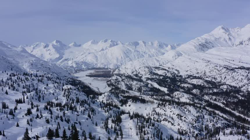 A stunning static shot captures the immense beauty of a snow-covered mountain valley under a clear winter sky