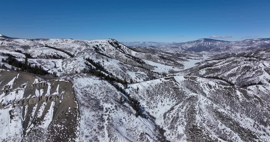 A stunning aerial view of a vast, snow-covered mountain range on a clear, sunny winter day