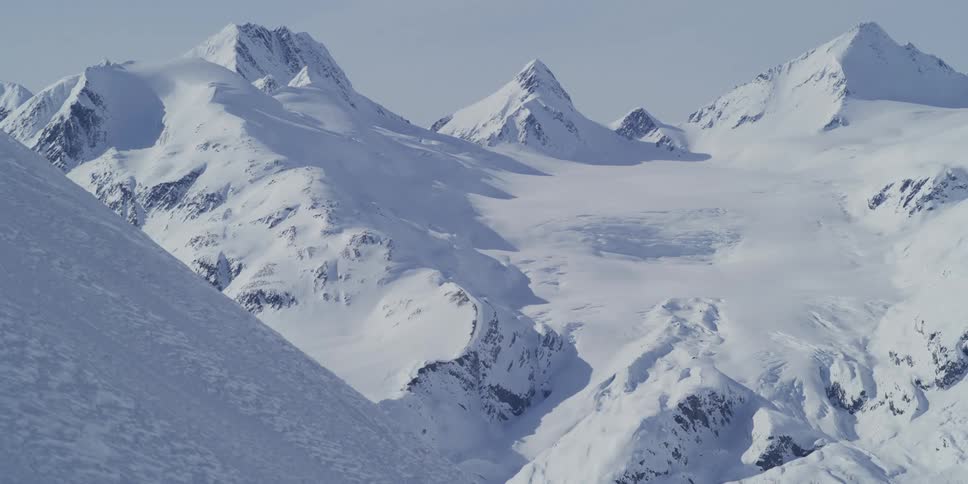 A majestic winter landscape shows a vast, snow-covered mountain range with glaciers under a clear sky