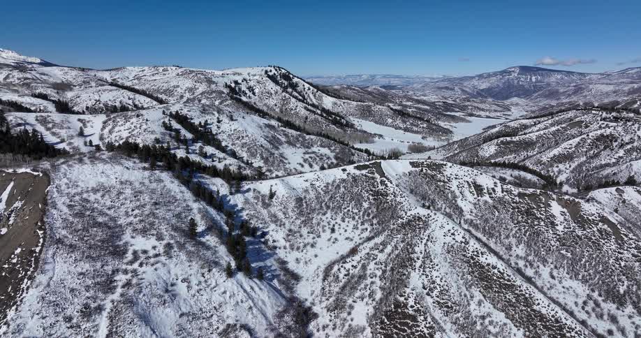 An expansive aerial view of snow-covered mountains and a frozen lake in a valley on a bright winter day
