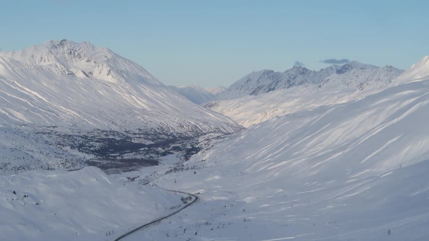 An expansive, majestic view of a vast, snow-covered mountain valley with a highway winding through it