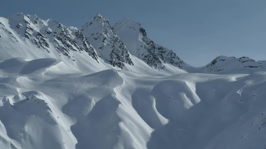 A vast and pristine snow-covered mountain range stands majestically under a clear blue sky on a sunny winter day