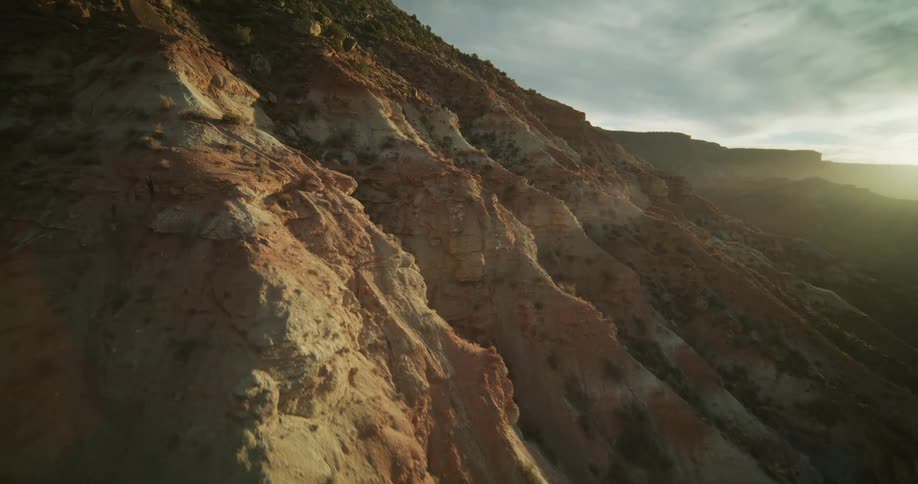 A dramatic aerial shot flies sideways along a rugged red rock mountainside at sunset