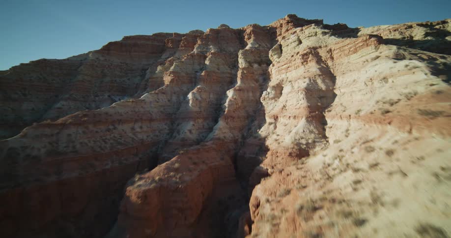 A dynamic aerial FPV drone flight soaring along the rugged, sunlit cliffs of a red rock canyon in the desert